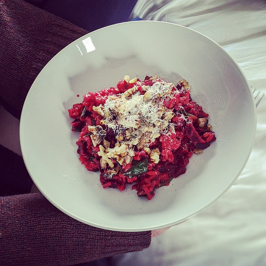 A white ceramic bowl containing a vibrant red beetroot risotto meal topped with walnuts and parmesan cheese