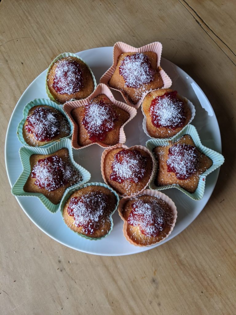Photo shows a plate of heart- and star-shaped fairy cakes topped with jam and coconut.