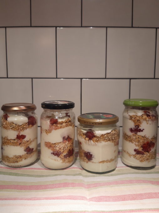 Image shows four jars on the worktop filled with a breakfast cranachan - yoghurt, oats and raspberries