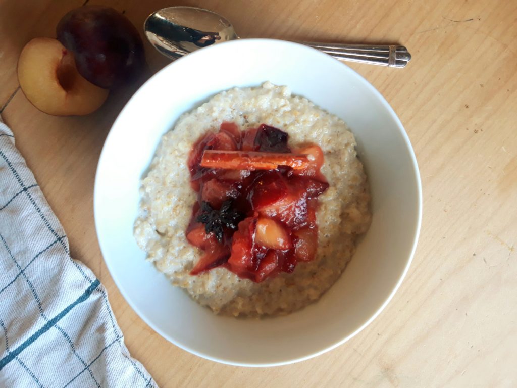 A photo of a bowl of porridge topped with purple poached plums.