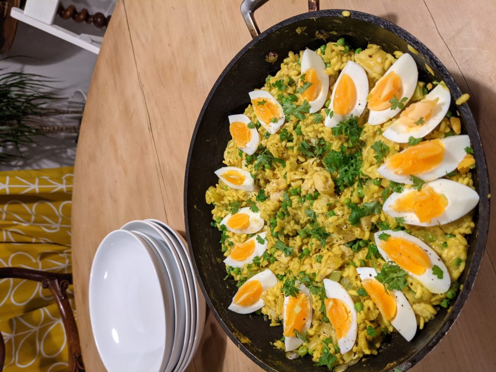 A table set for serving with white plates and a large cooking pan full of spiced, herby rice and quatered boiled eggs
