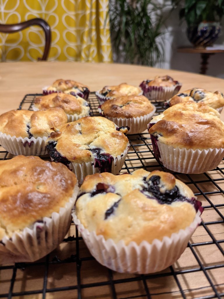 Freshly baked muffins set to cool on a drying rack laid on a pine table