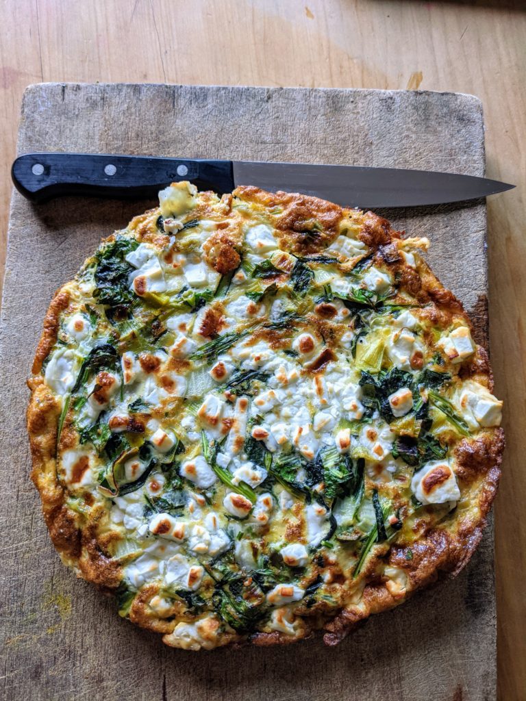 A large round colourful feta and herb frittata set on a wooden chopping board 