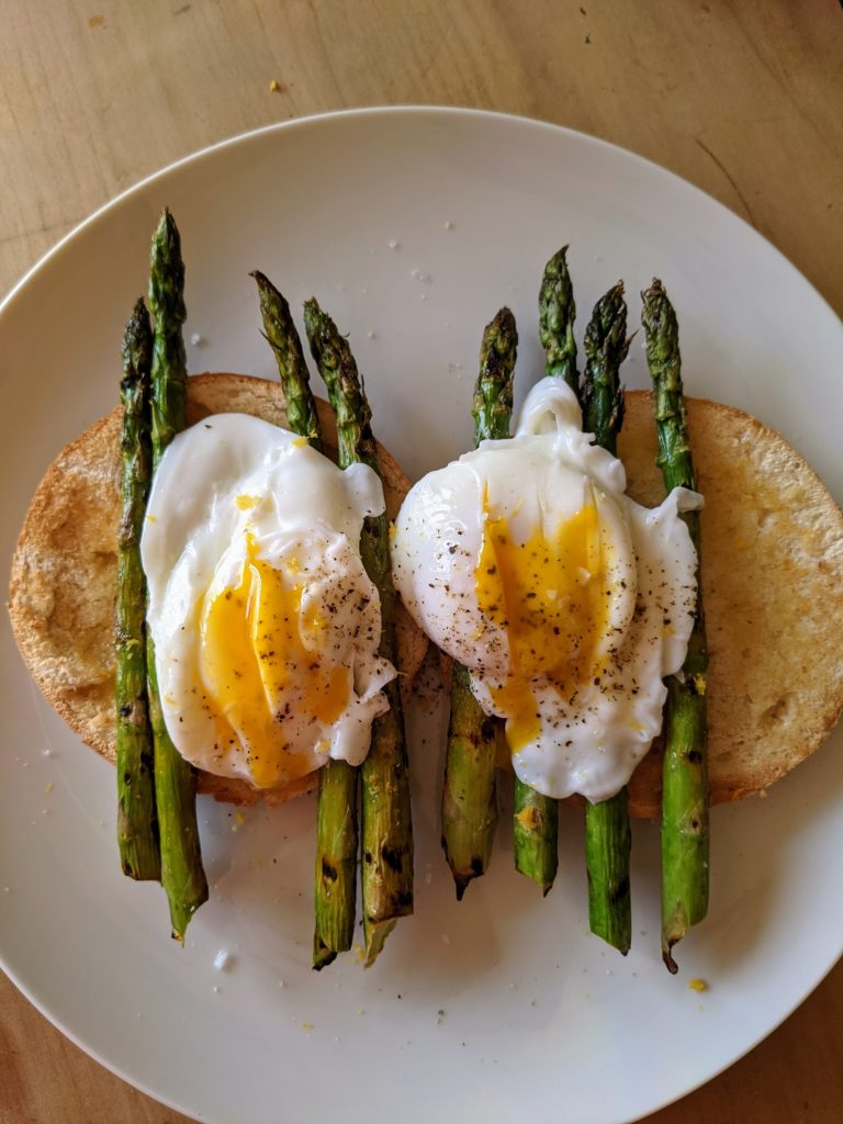 A white plate set with toasted bread, griddle roasted asparagus and poached eggs