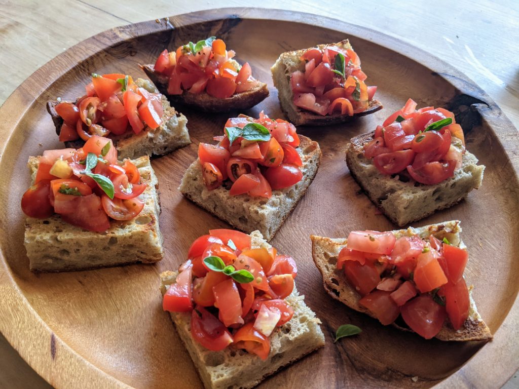 A wooden platter set with a number of small squares of tomato bruschetta