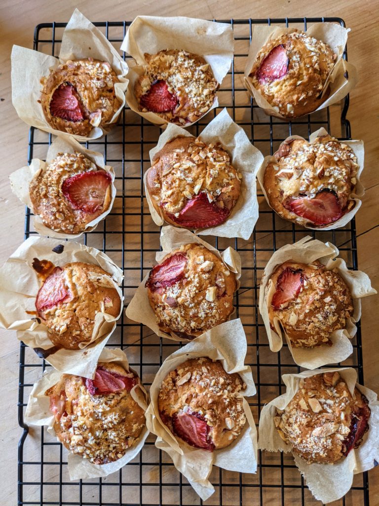 A black cooling tray on a pine table set with freshly baked strawberry and almond muffins.