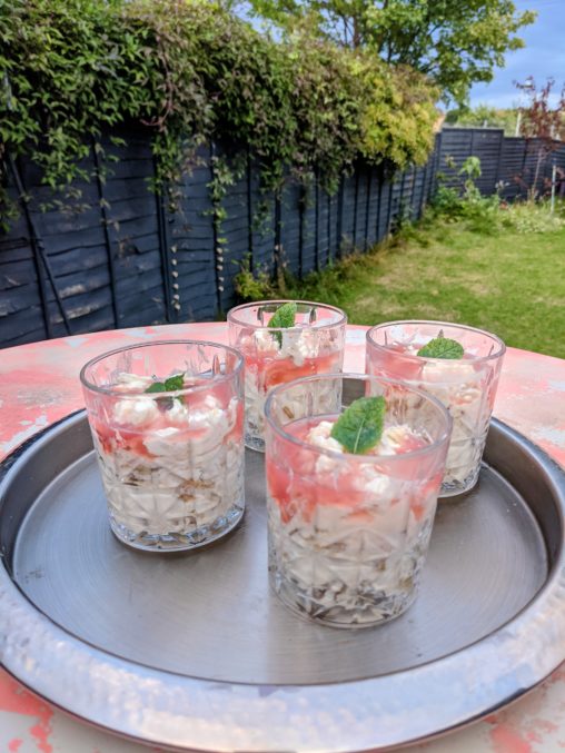 A silver tray on a pink table in the garden, served with 4 glasses filled with rhubarb fool and topped with a bright green mint leaf.