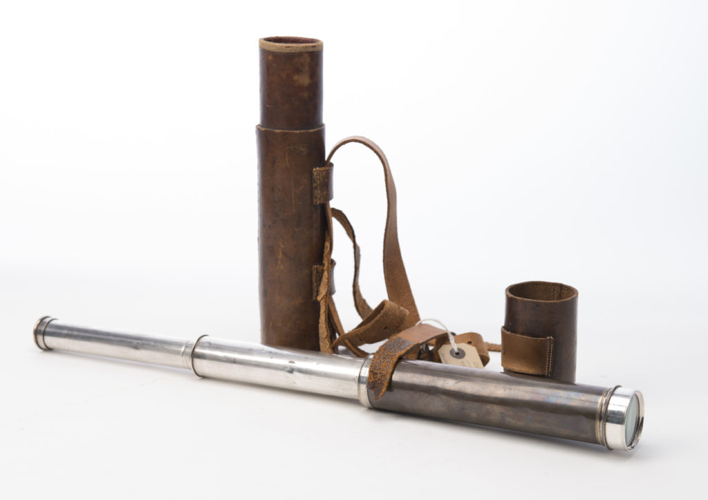 A telescope, partially extended, alongside its leather case with straps.