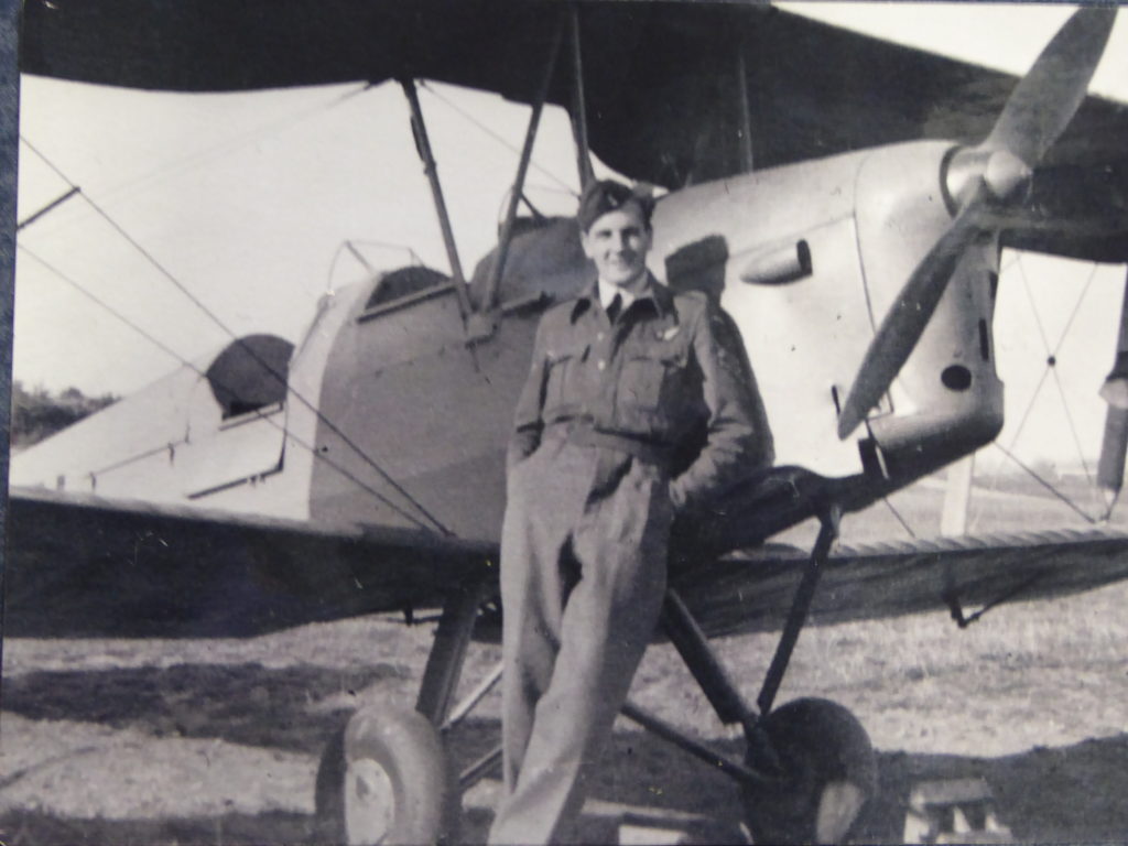 Black and white photograph showing Ross Eudall in his RAF uniform leaning against a small plane with a propellar.