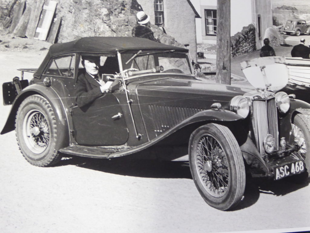 Black and white photograph showing Ross Eudall inside a vintage car.