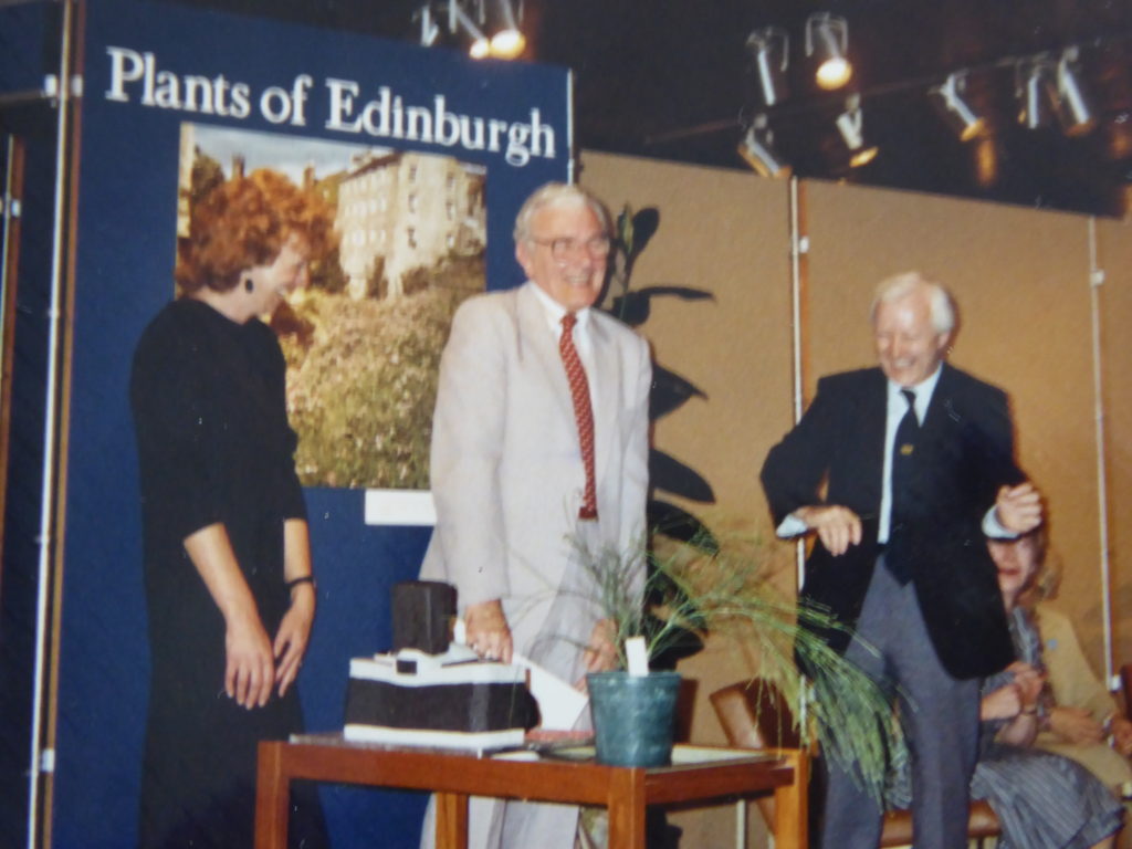 Colour photograph showing Ross Eudall smiling at his retirement party. His cake is in the shape of a camera.