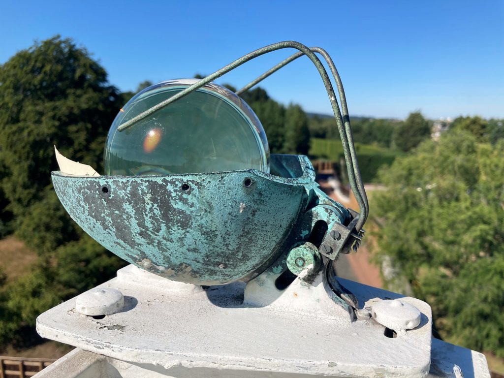 Campbell-Stokes sunshine recorder sits in its cradle on a plinth on a sunny day