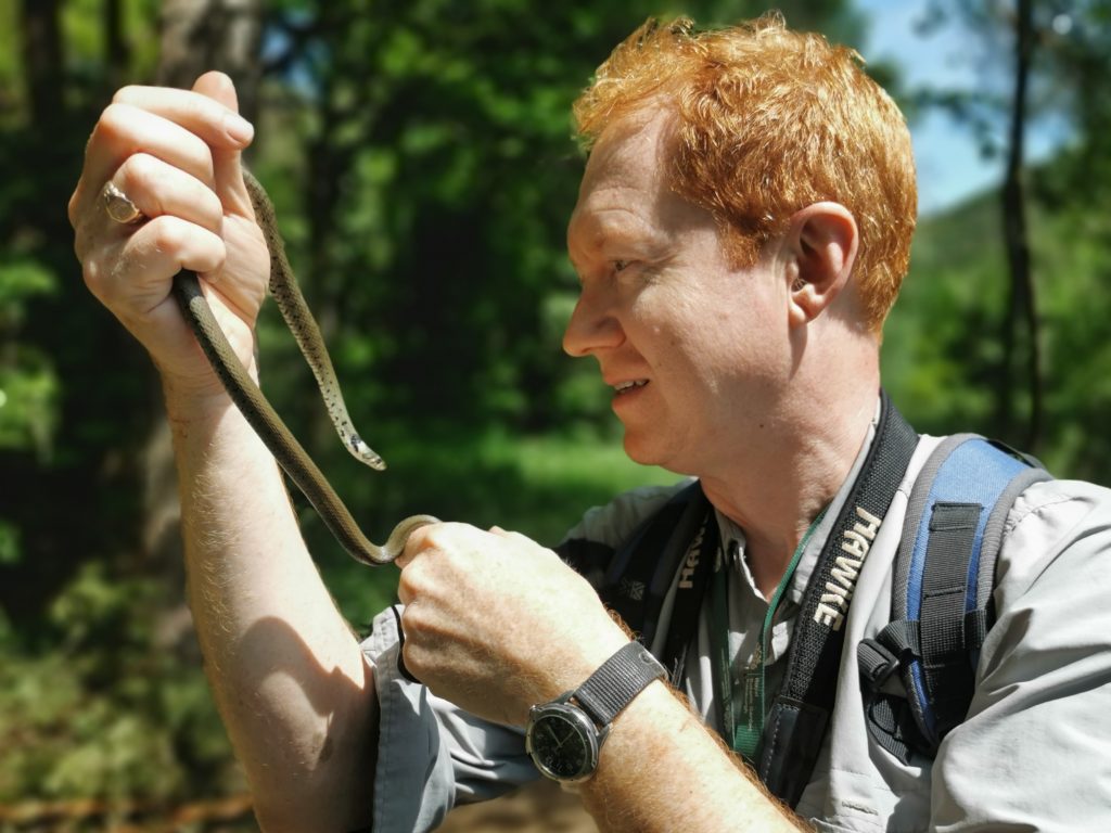 A white man in side profile holding a snake