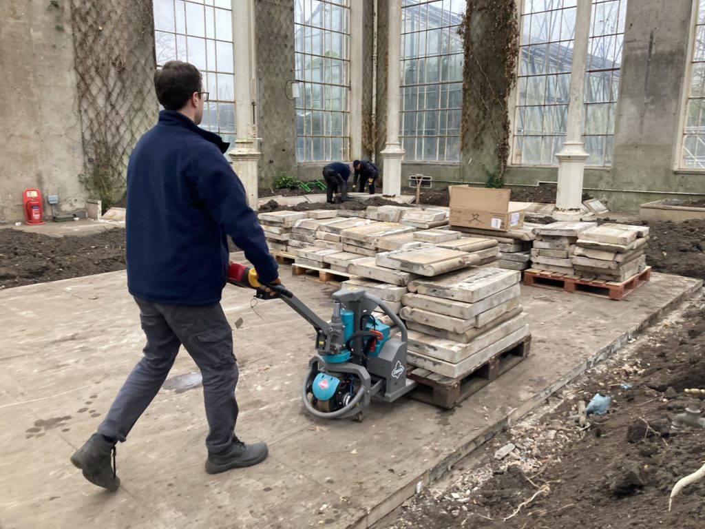 Person with pallet truck pushes a pallet of stone slabs inside a Victorian glasshouse