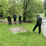 in a rain storm in a garden, a large water blister under a lawn is inspected by one person while three take pictures
