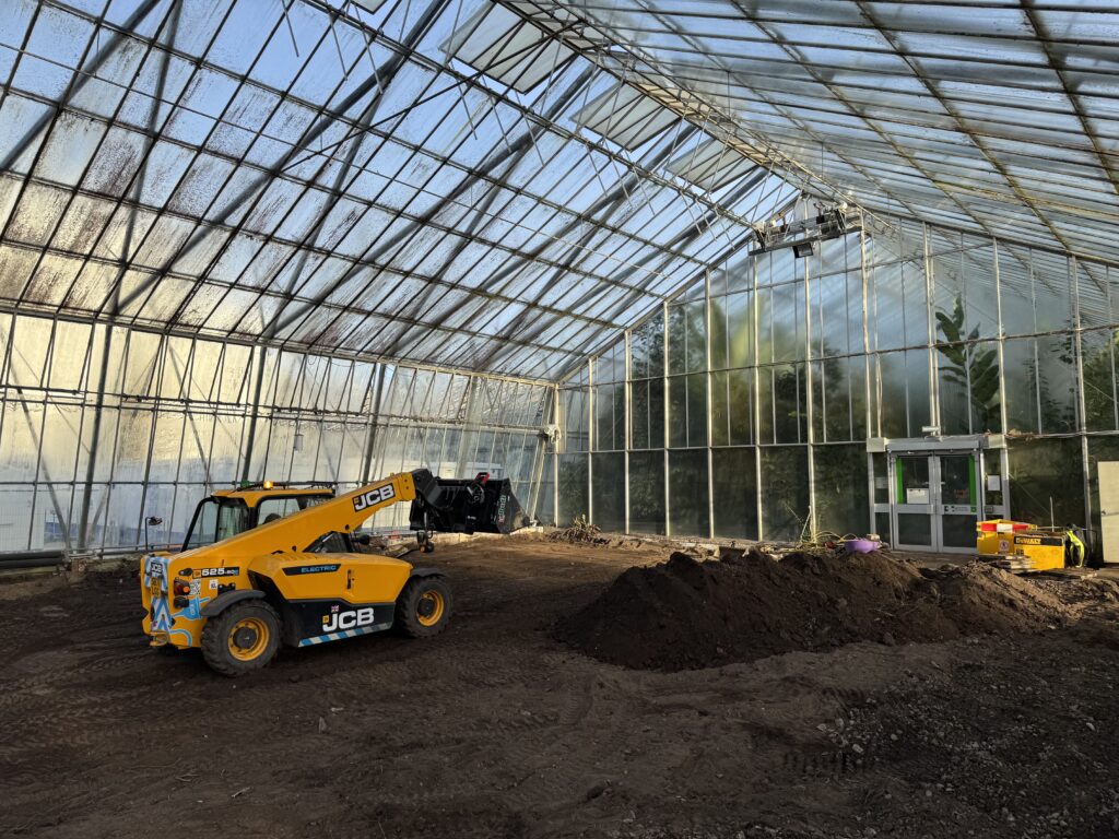 An electric telehandler moves soil in a glasshouse