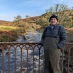 Man standing on bridge above a highland burn