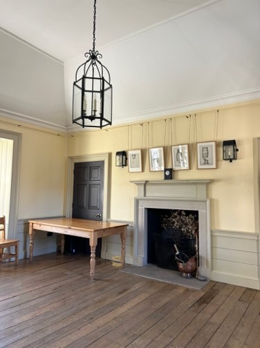 Image showing corner of large room, with pictiures on wall above fireplace, table in corner against a door and a centre lantern light fitting hung from the ceiling