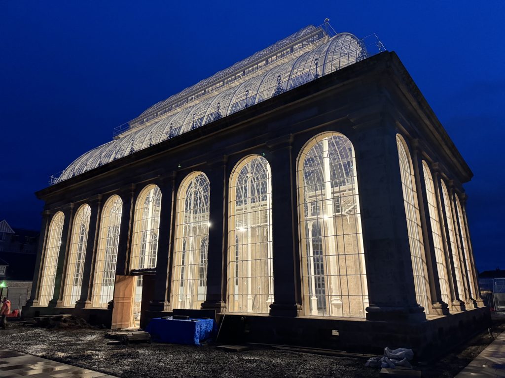 The Palm House during a dark morning, inside lights illuminate the structure.