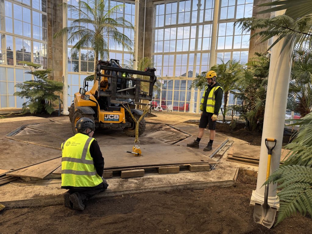 Two men position heavy steel plates used to protect the ground inside the Palm House.